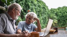 An older married couple sits outside with a laptop computer.