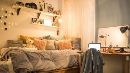 A dorm room with a bed filled with cushions and fairylights