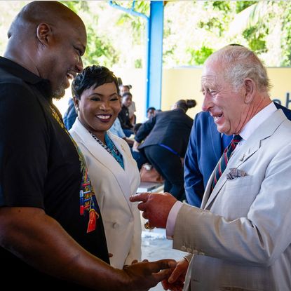 King Charles laughing and pointing at a man's shirt in the Bahamas