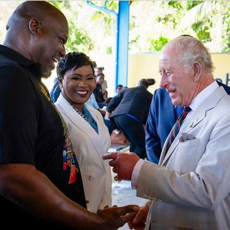 King Charles laughing and pointing at a man's shirt in the Bahamas