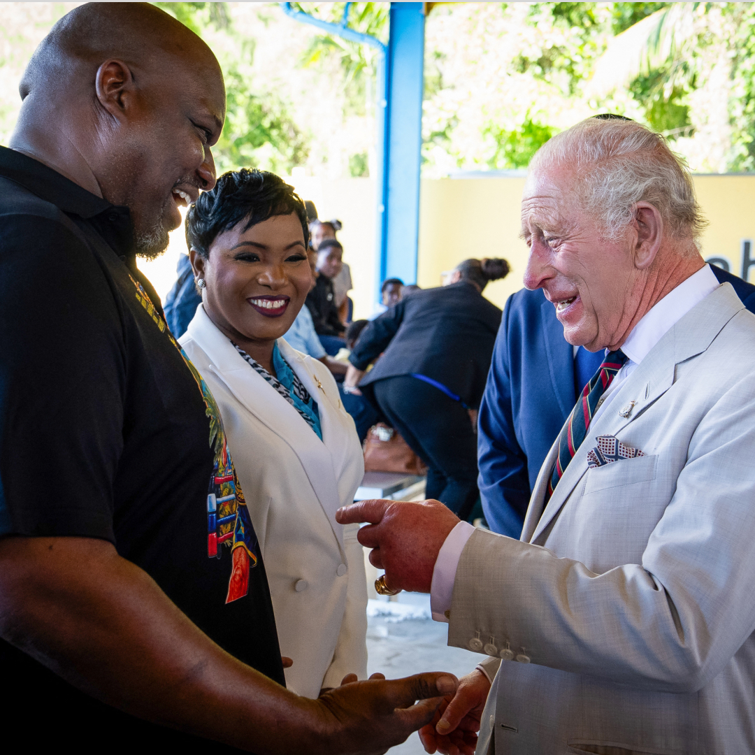 King Charles laughing and pointing at a man's shirt in the Bahamas