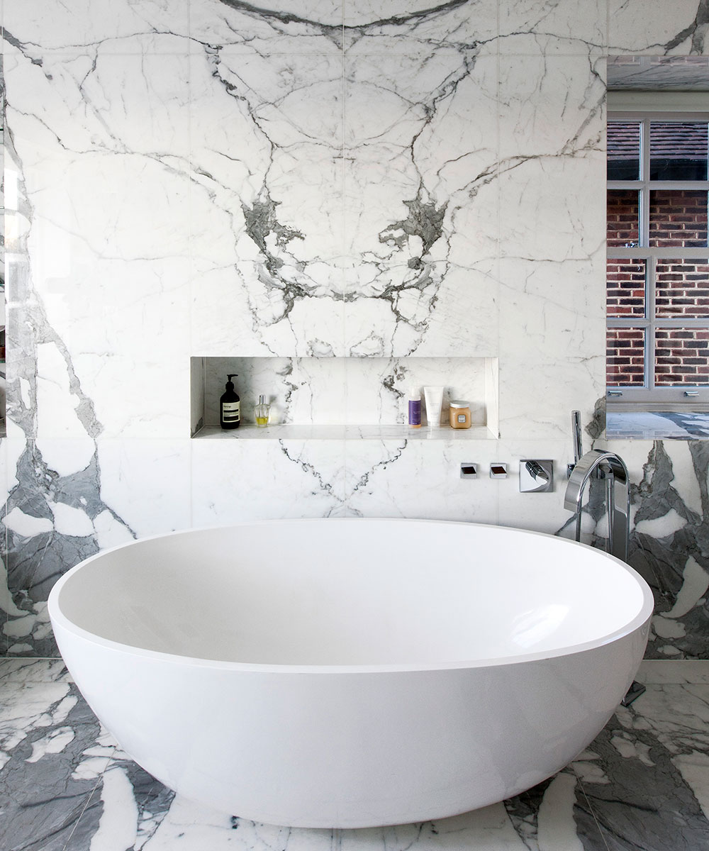 A large bath tub in a white marble bathroom, one of 2021's key bathroom trends.