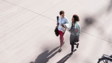 Two women walking together and laughing in the city on a concrete path, after learning is 10,000 steps a day good