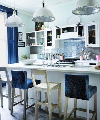 A white breakfast bar with blue and white bar stools below three industrial metal pendant lights