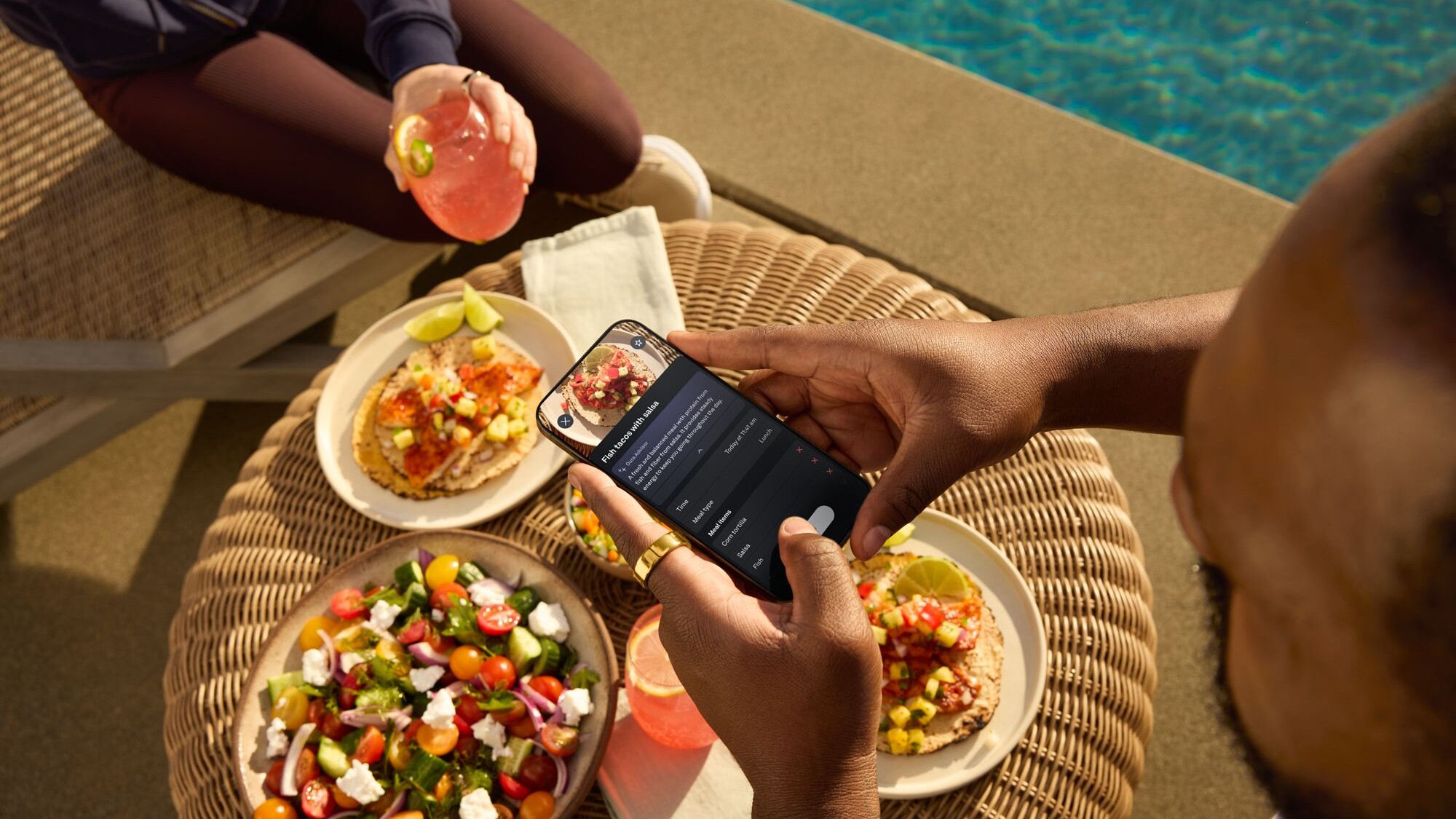 Table of food next to a swimming pool with person taking photo on their phone using Oura meal feature