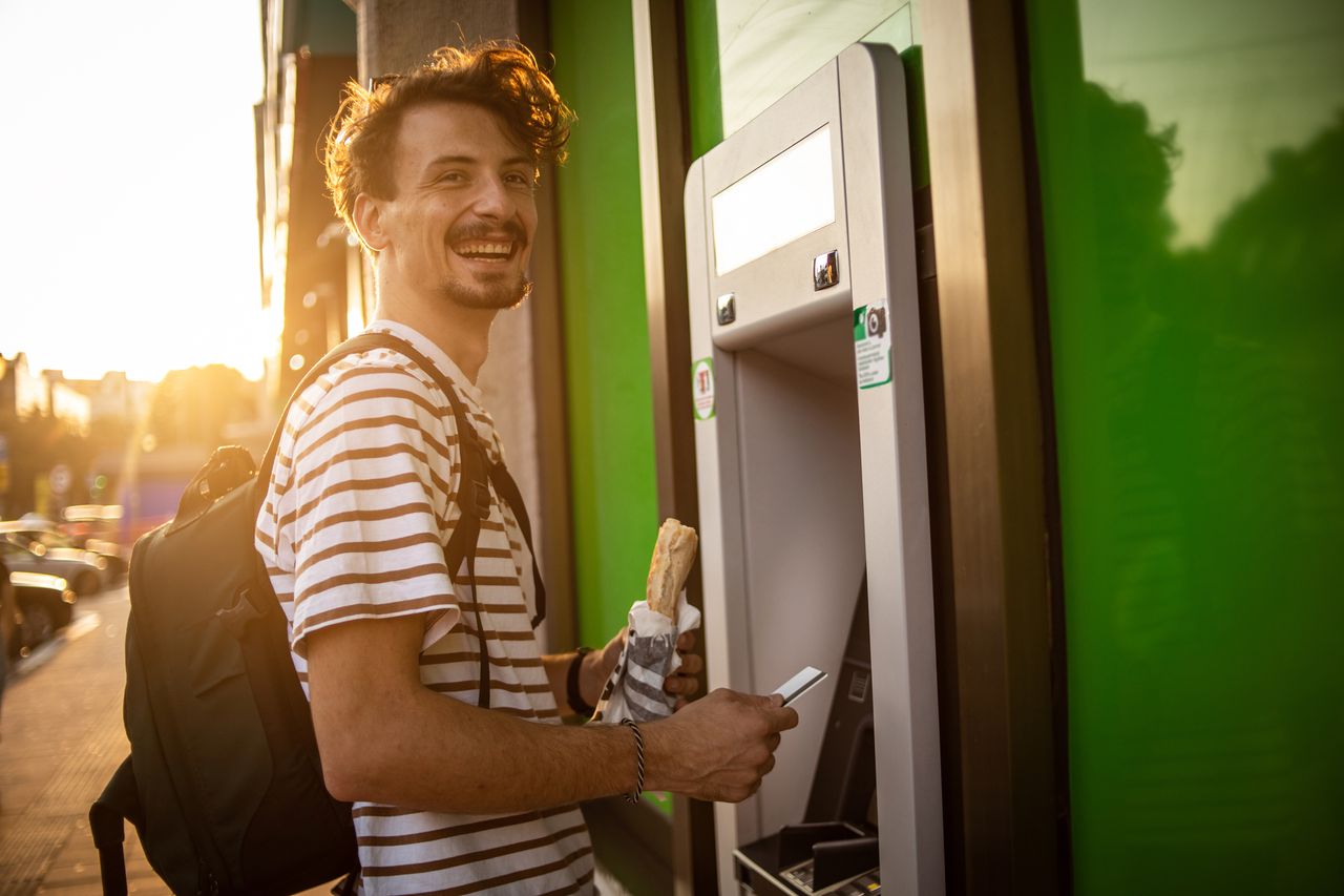 A young man uses a debit card at an ATM machine