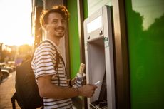 A young man uses a debit card at an ATM machine