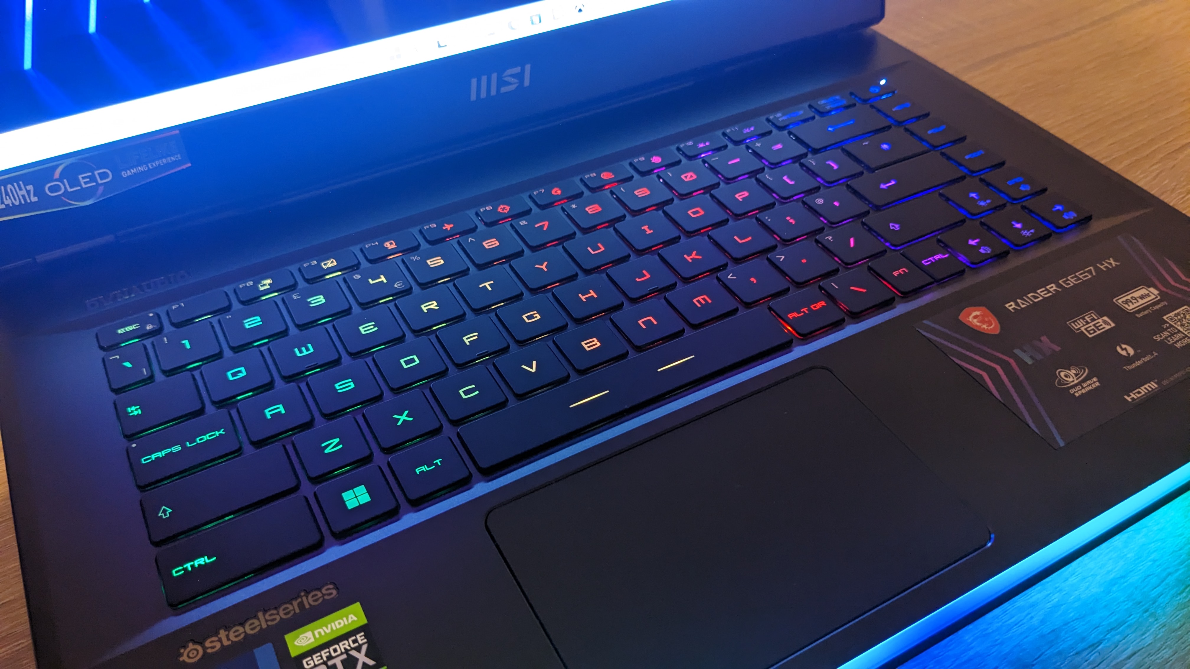 The MSI Raider GE67 HX photographed on a wooden desk with RGB lighting turned on.
