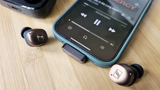 The Questyle QCC Dongle Pro with a smartphone to denote size, on a light wooden table