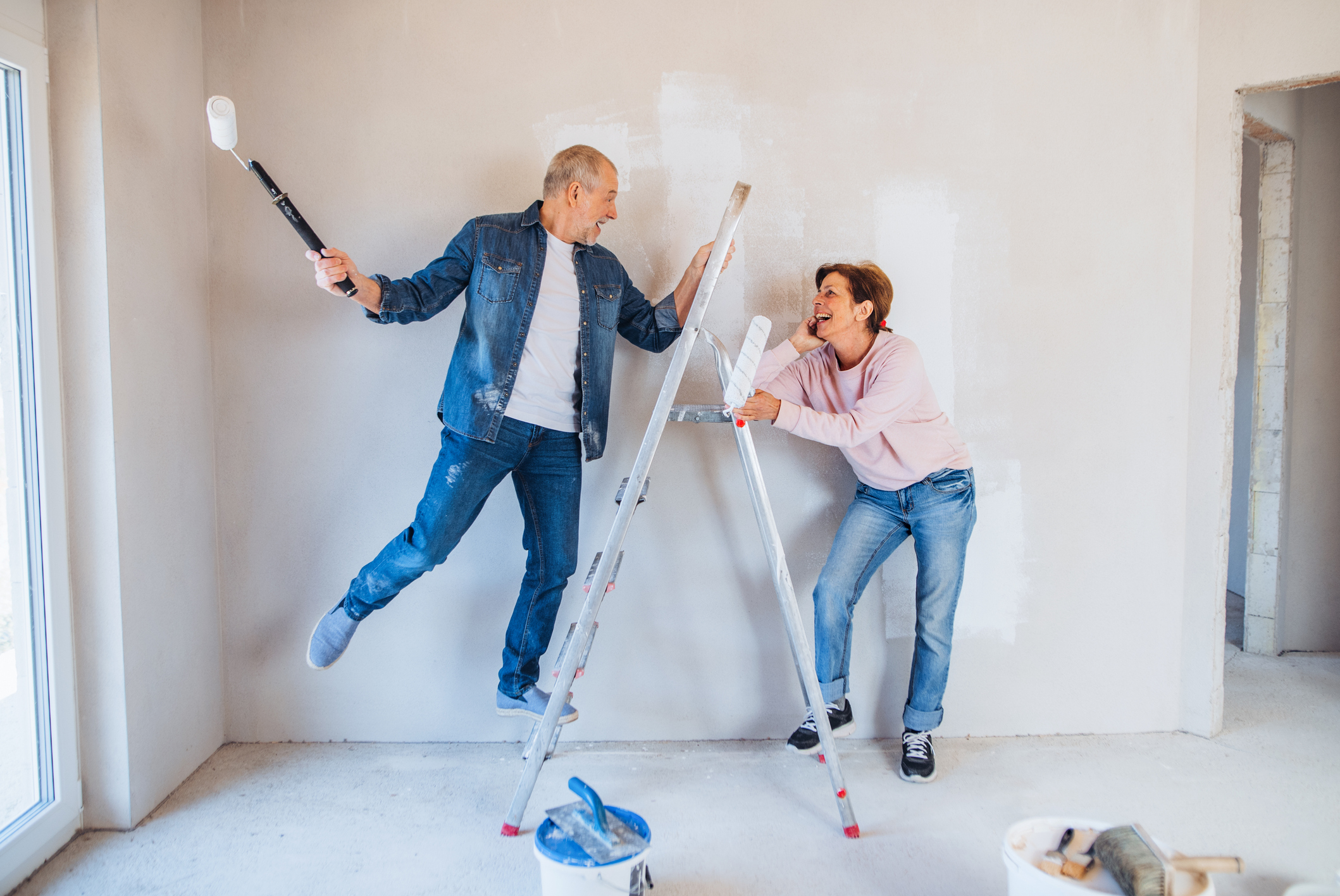 A couple painting walls and renovating their home, having fun. 