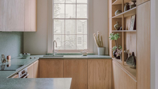 an extremely small, sleek kitchen design with light oak cabinetry, without handles, and a dark green terrazzo counter and backsplash.