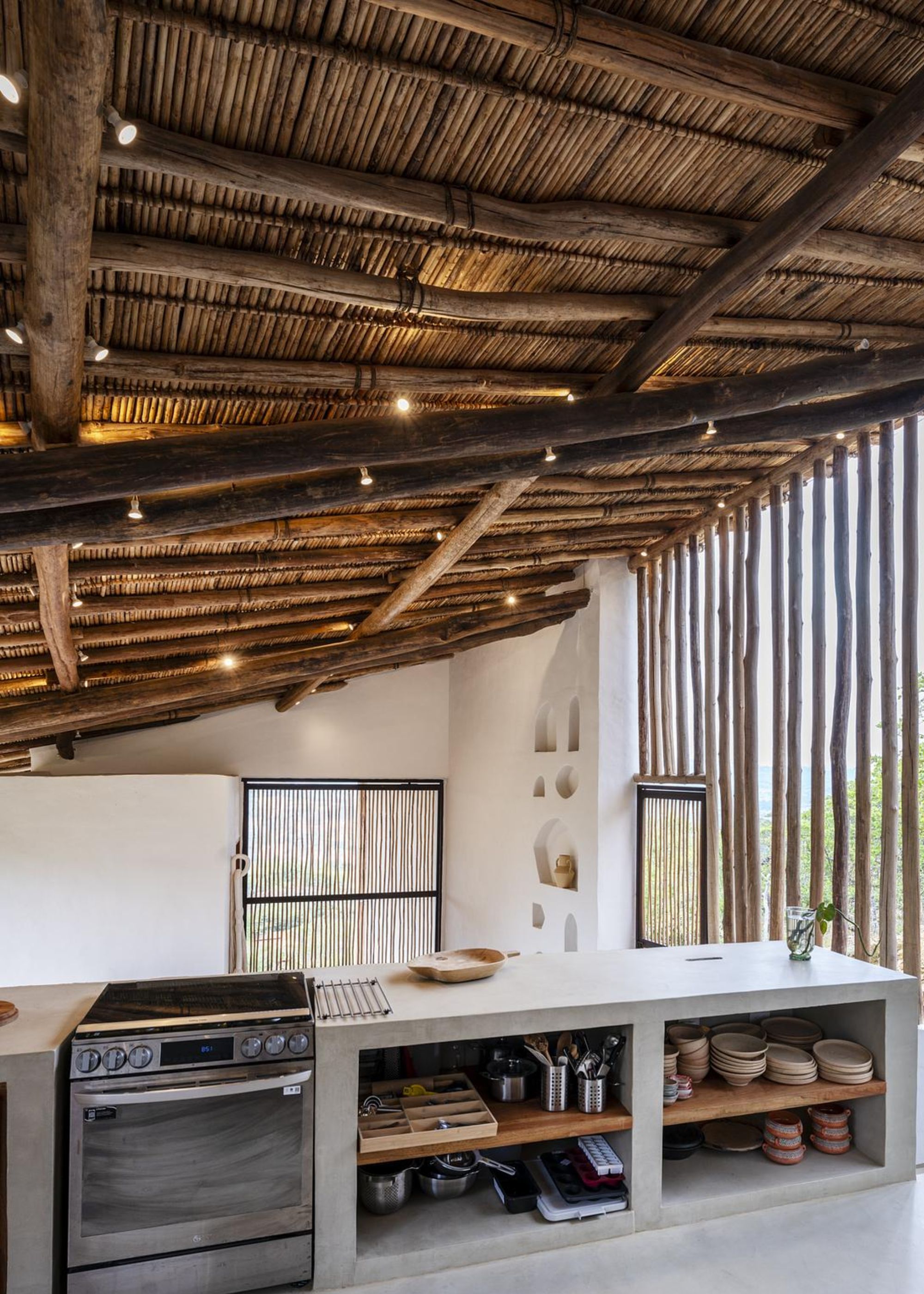A kitchen with concrete worktops as well as open shelving in the kitchen with a view of kitchen dishes. There is also an oven with a stove top.