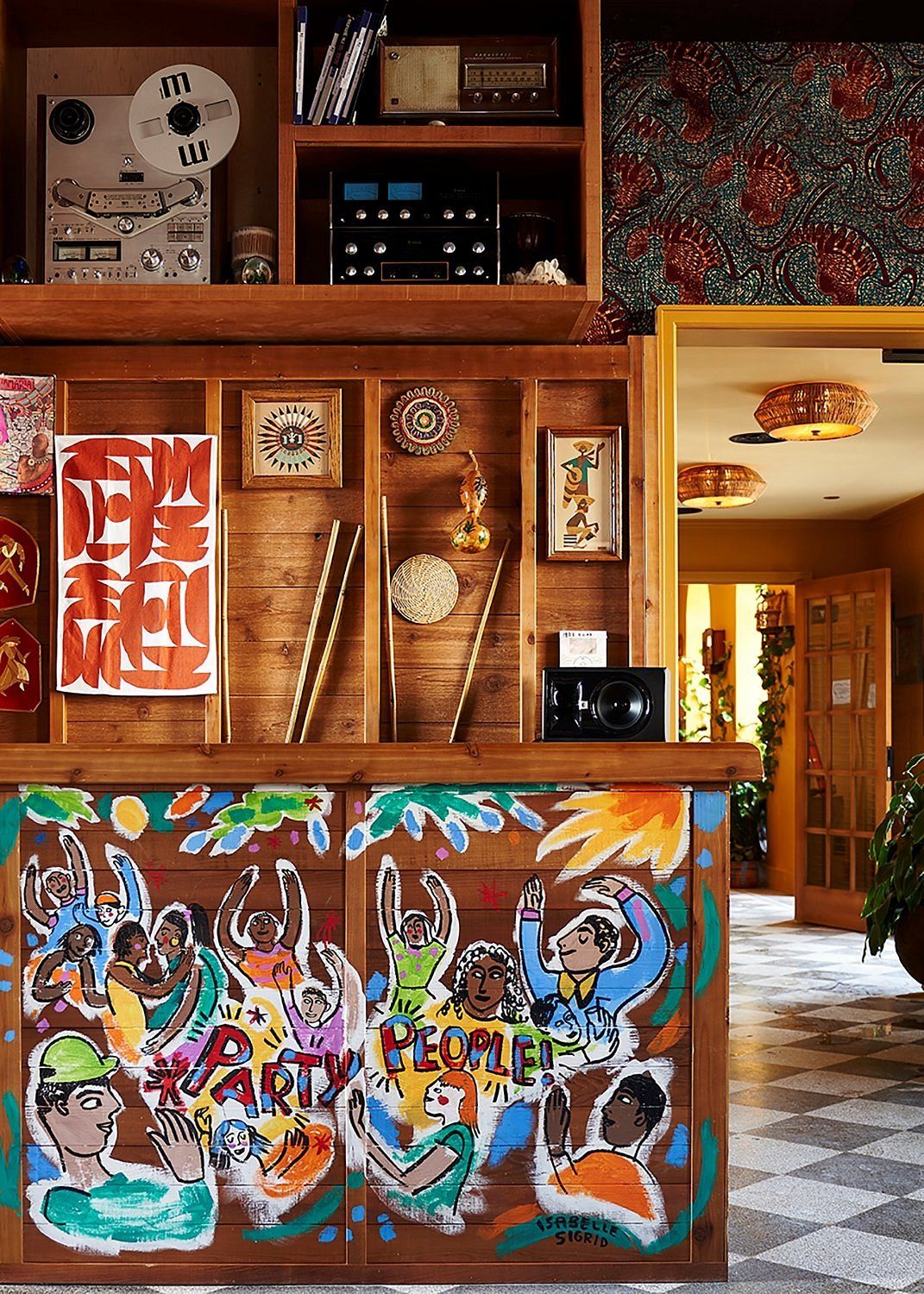 A wood and murals-clad hotel bar features a music culture-inspired aesthetic, with mosaiced floors, stacked-up shelves, and vintage collectibles scattered throughout.