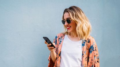 Smiling blond woman using smartphone, blue background - stock photo