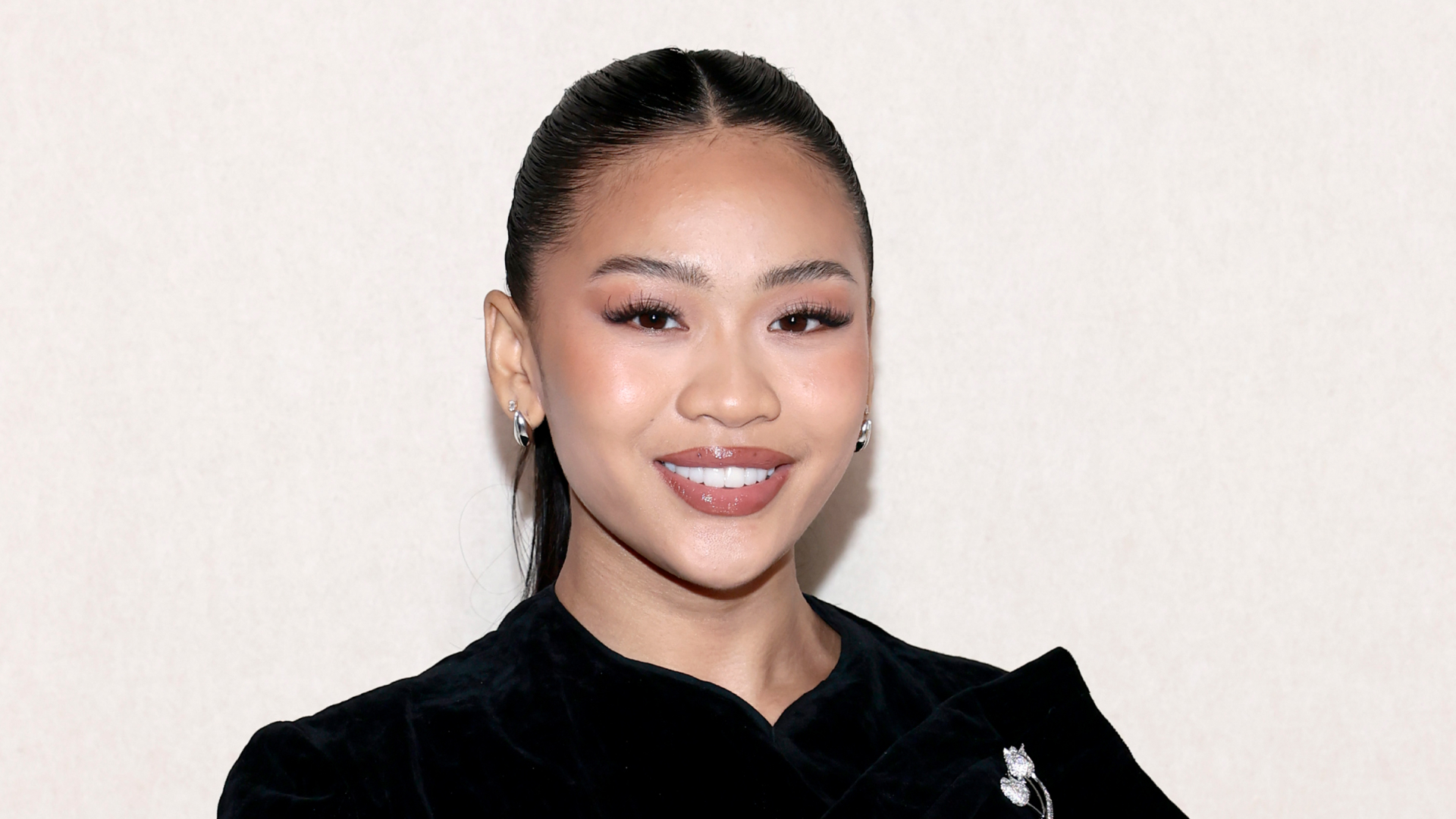 Gymnast Suni Lee wearing a ponytail hairstyle, soft skinlike makeup and a black top. She is smiling at the camera