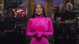 Kim Kardashian speaking during her monologue on Saturday Night Live, dressed in a pink jumpsuit.