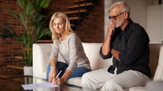 A married senior couple sits on a couch discussing their finances.