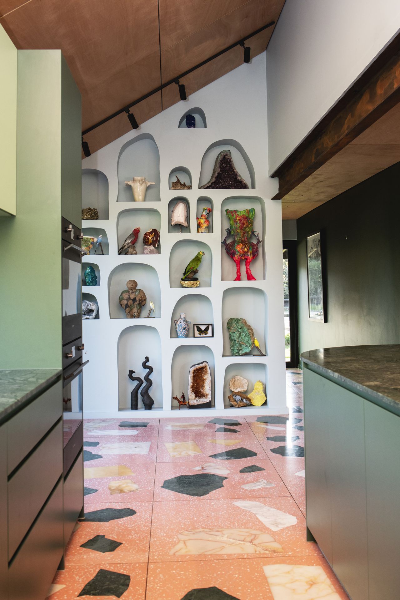 colorful kitchen with colored stone floor, green cabinets, and light blue alcove shelves with sculptures in each alcove