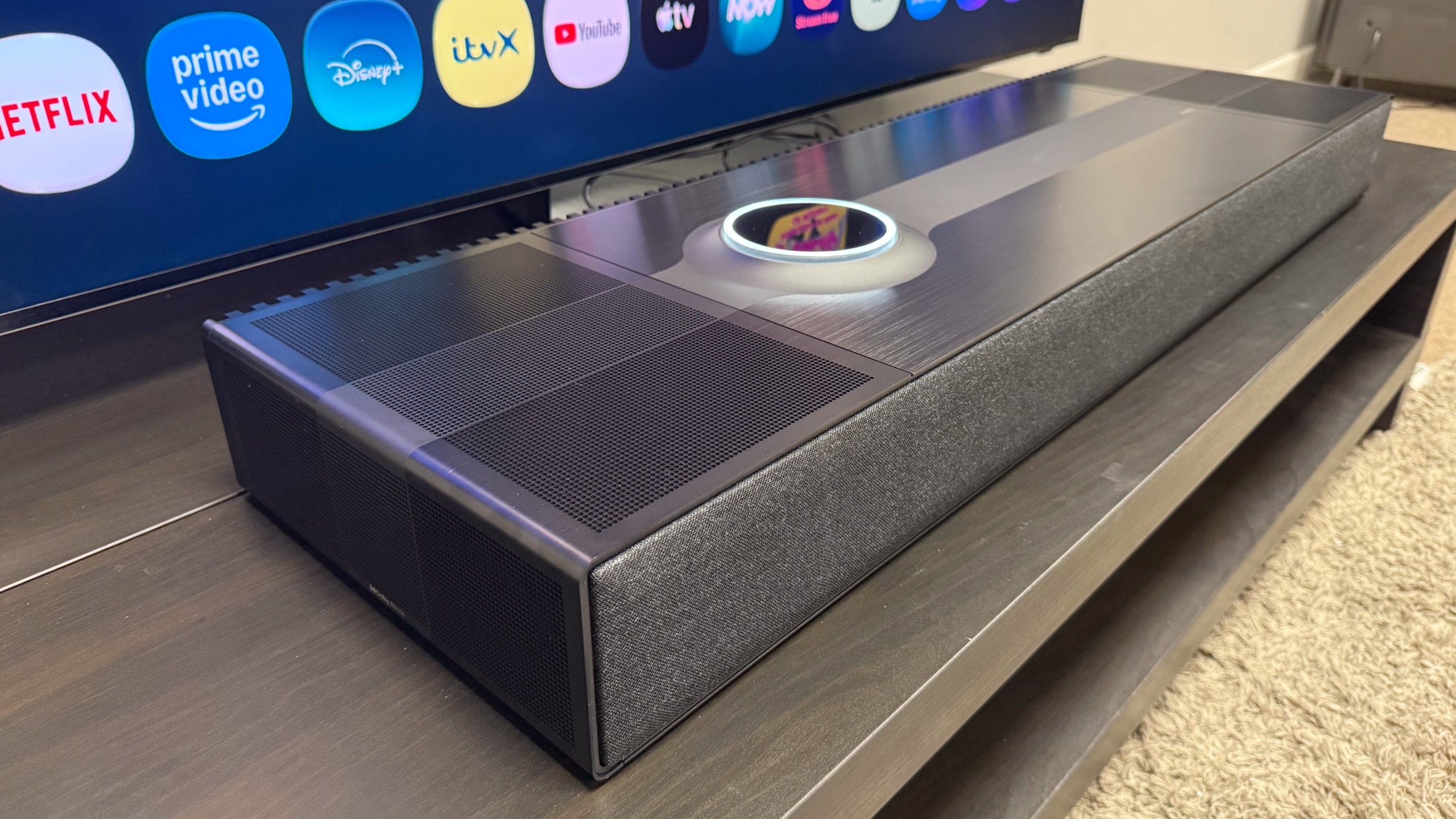 The Focal Mu-so Hekla at a 3/4s angle showing the Samsung R95H TV's home screen menu reflected in the dial.