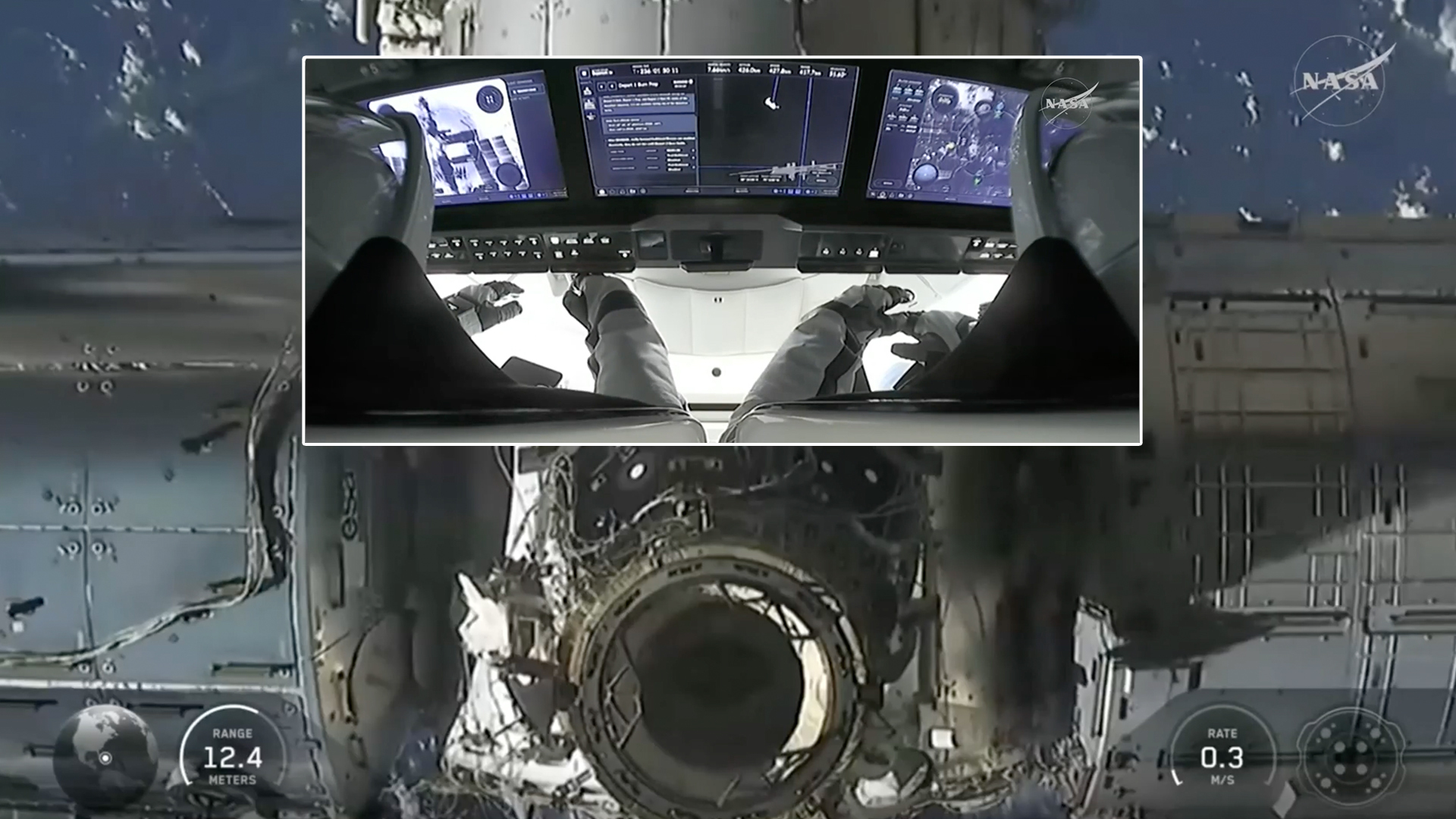 an over-the-shoulder view of two people in white space suits sitting very close to a bank of screens showing spacecraft controls and telemetry