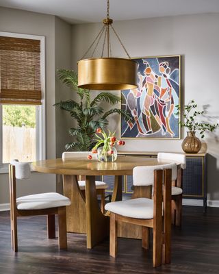 A dining room with a round table, boucle chairs, and a brass lamp shade overhead