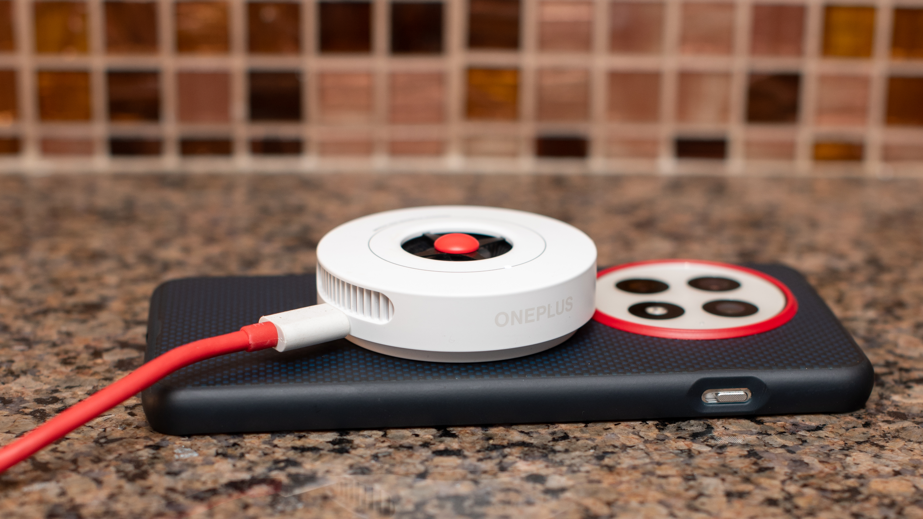 OnePlus 13 with aramid fiber case and AirVOOC charger on top, laying on marble counter