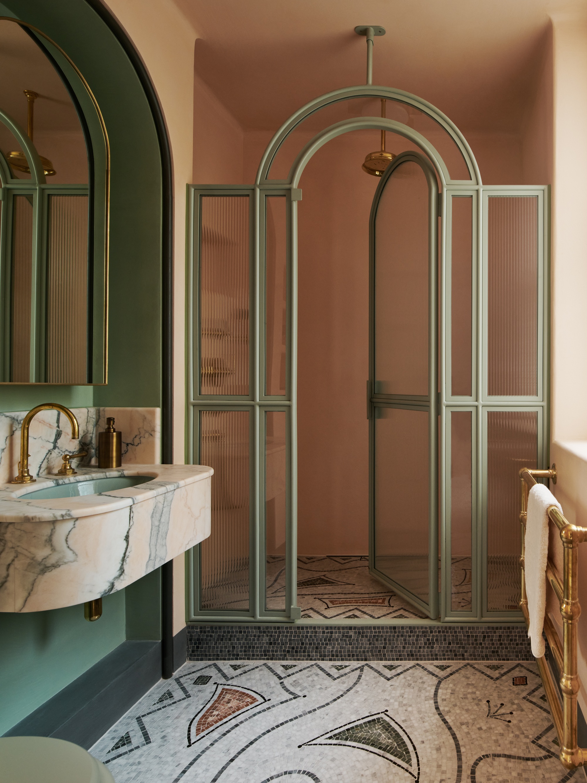 an art deco bathroom with a mosaic decorative floor, and an arched shower screen with pink and green color palette