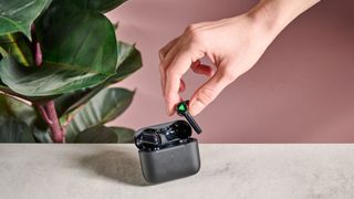 Hand holding Razer Hammerhead Pro HyperSpeed earbud on table with pink and plant in background