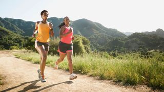 Woman running in a couple across the trail with mountains in the background