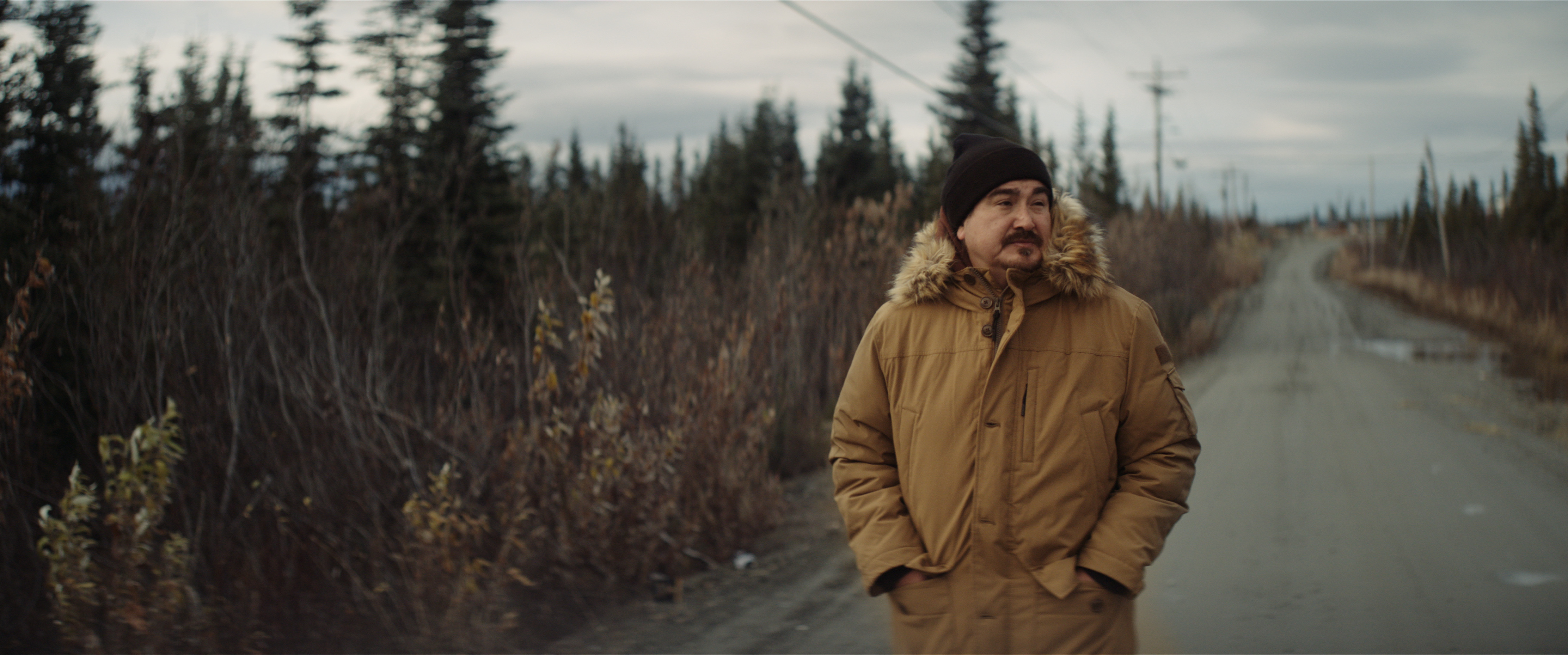 JAMES DOMMEK JR. wearing a brown coat walking down a road surrounded by trees in blood and myth