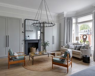Pale grey living room ideas illustrated in a mid-century scheme with statement chandelier light and wooden furniture.