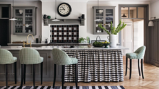 a kitchen with a black and white printed counter skirt, green barstools, gray cabinets, and a vase of green plants on the counter