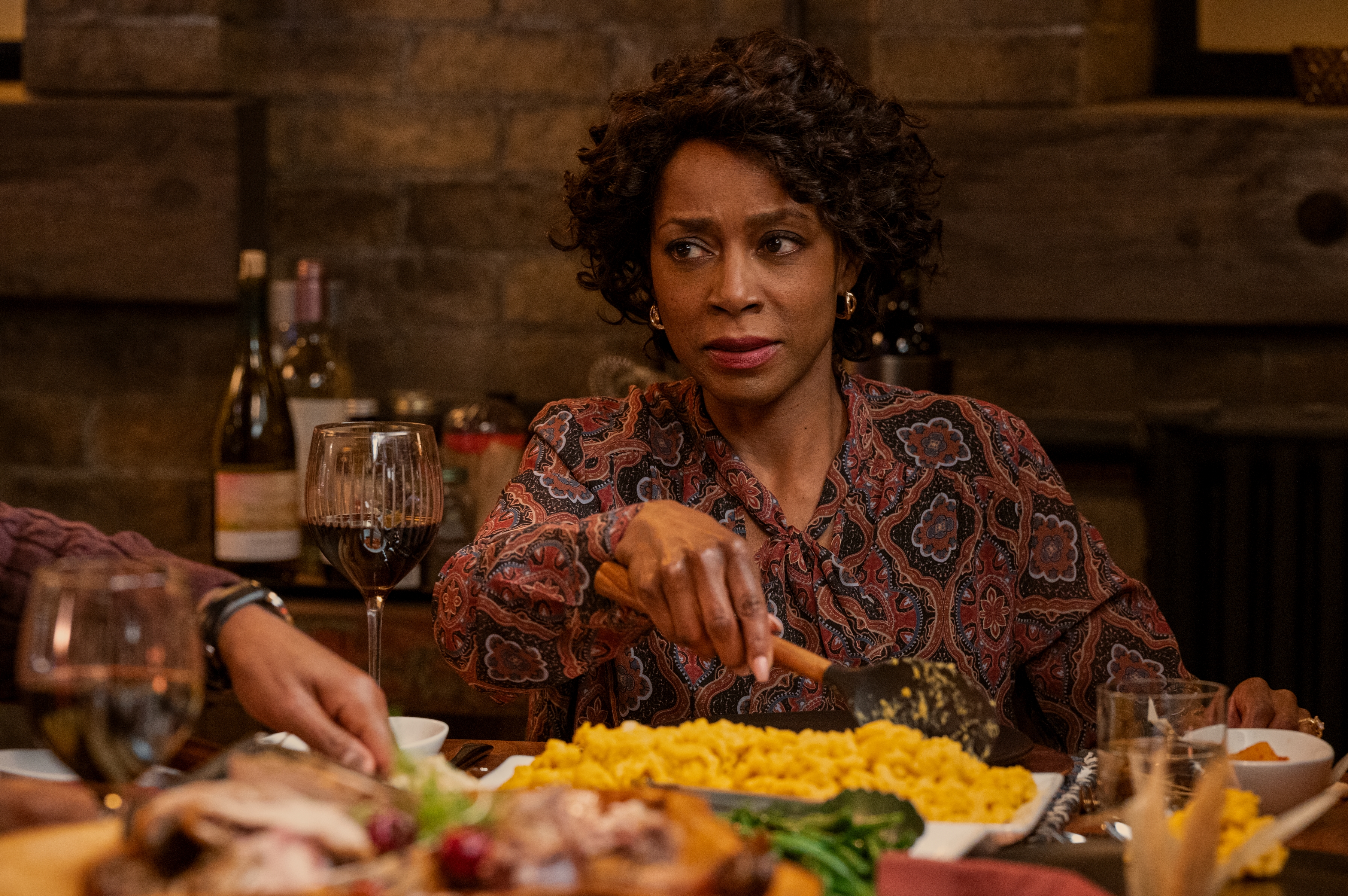 Karen LeBlanc as Lynette, sitting at a dinner table in front of turkey and macaroni and cheese, in episode 201 of Ginny & Georgia.