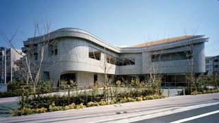 Frontal view of contemporary building with patterned concrete walls and curved corners, with planting in the foreground.