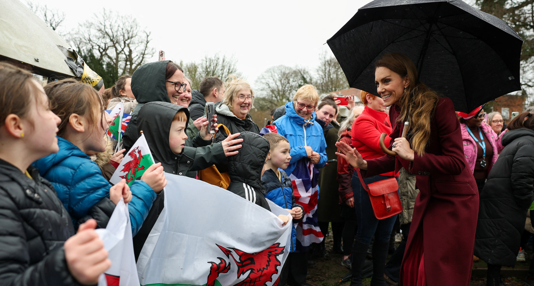 Princess Kate holding an umbrella talking to fans in the rain