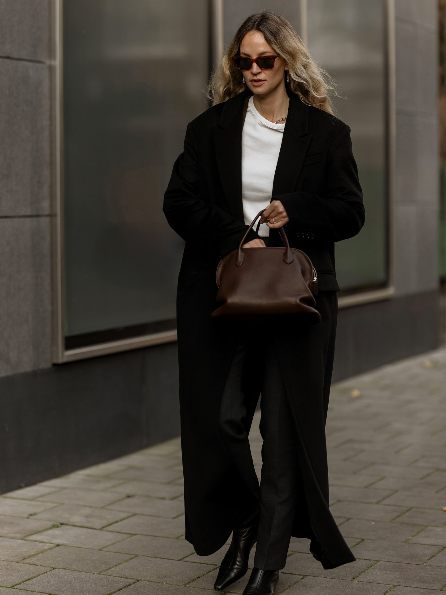 Anouk wears a black jacket, white tee, black jeans, black boots, and a brown bag.