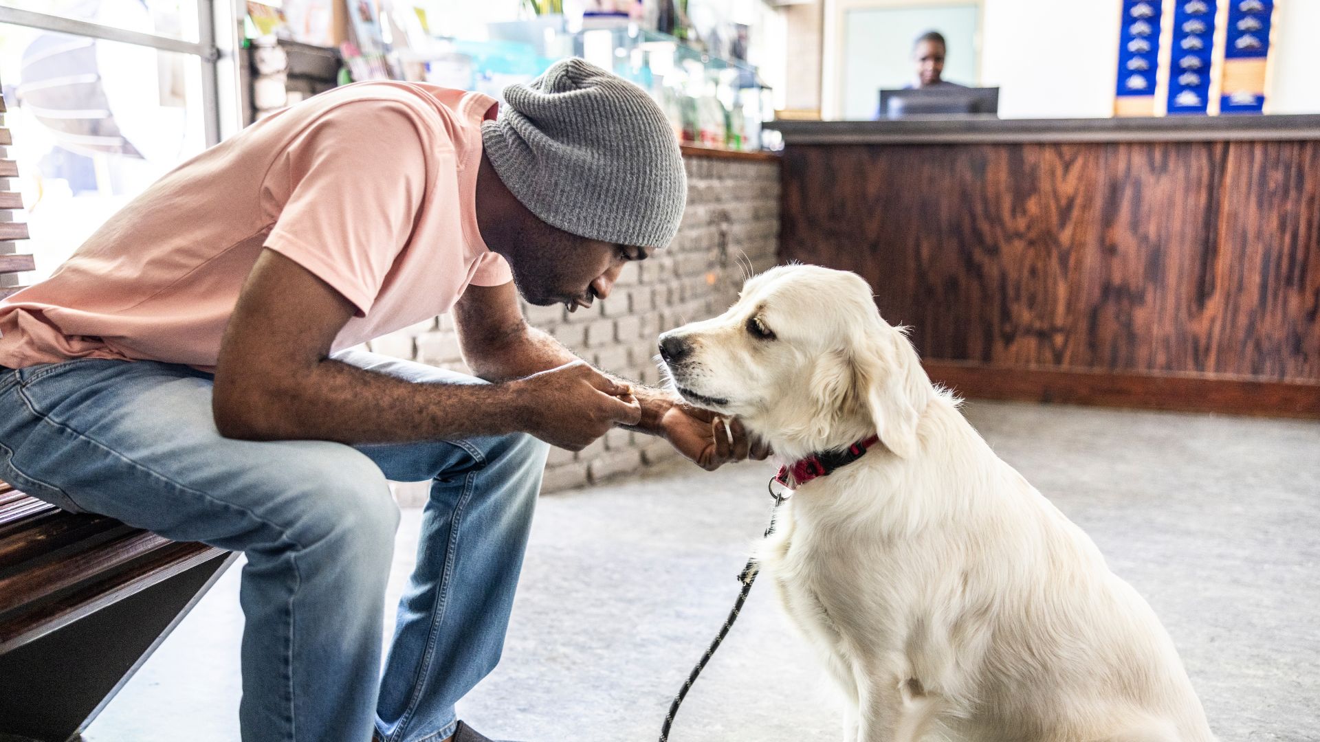 Man in a grey beanie and pink top speaking to his white dog