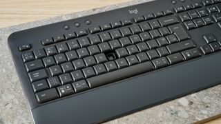 a black full sized keyboard with batteries and a palm rest on a clean beige surface with a blue backdrop