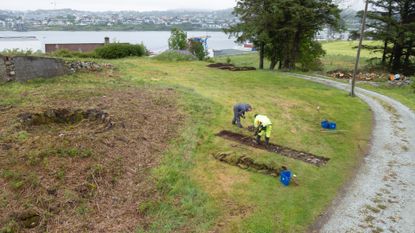 Here this photo shows an aerial view of two people digging on the burial ground (a grassy area free of trees or shrubs).