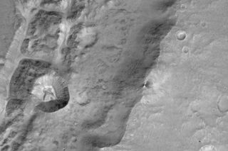 Image of a 0.9 mile-size (1.4 kilometers) crater (left-center) on the rim of a larger crater near the Mars equator. It was acquired at 7.2 meters/pixel by the Colour and Stereo Surface Imaging System (CaSSIS) aboard the European Space Agency's ExoMars Trace Gas Orbiter.