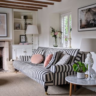 A living room with a striped sofa and a built-in bookcase in the alcove painted a darker shade of off-white set against white walls