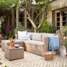 A rattan-effect garden sofa with light grey cushions on a contemporary patio