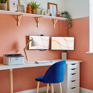 Orange and white two toned painted wall, white desk, dual monitor computer setup, blue desk chair, shelving