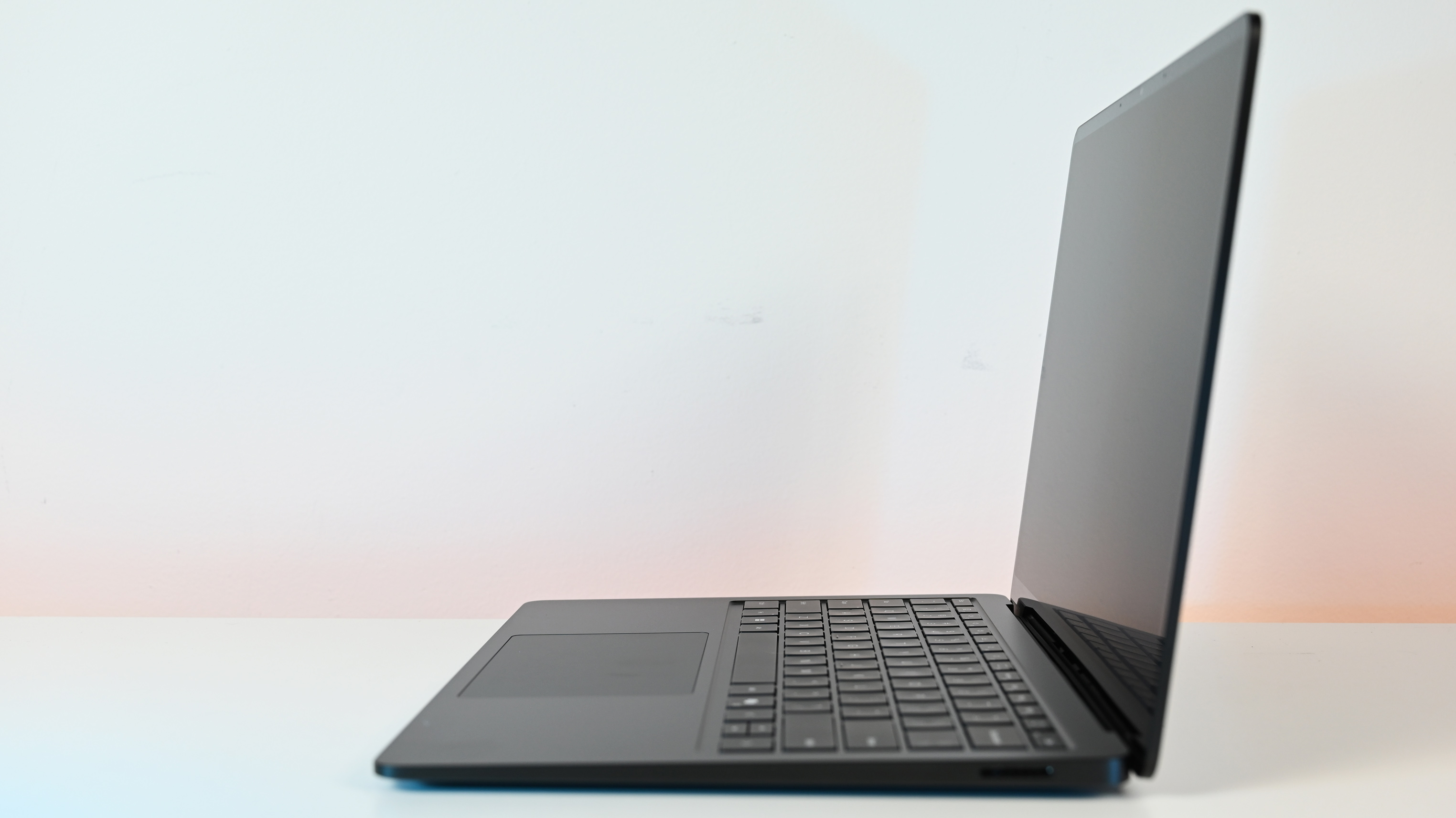 A sleek laptop with a black keyboard and a modern design, displaying a blue abstract swirl on its screen, set against a light gradient background.