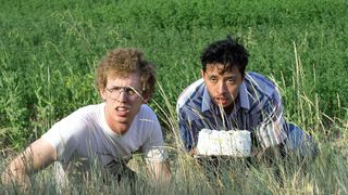 (L, R) Jon Heder as Napoleon Dynamite and Efren Ramirez as Pedro Sánchez, crouched in tall grass, in Napoleon Dynamite