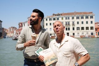 Rylan holding an ice cream and Rob holding two Grand Tour books as they stand in front of the Grand Canal.