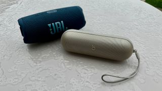 Beats Pill and JBL Charge 5 sitting on a wet table outside