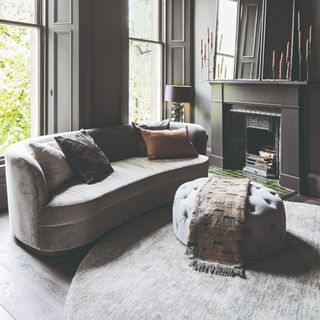 A grey living room with a curved grey sofa and a coordinating round ottoman and round grey rug