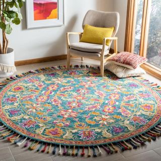 A round multi-colored rug is in a living room with a wooden chair on top of it