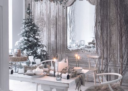 An all-white dining room decorated for Christmas with a flocked Christmas tree in the corner